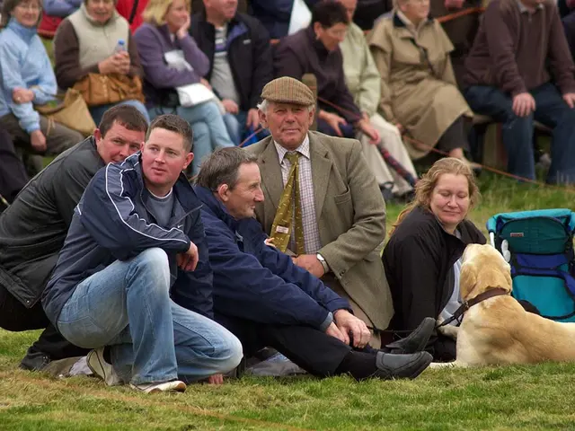There are few people sitting in front of a dog and the ground is greenery and there are few people...